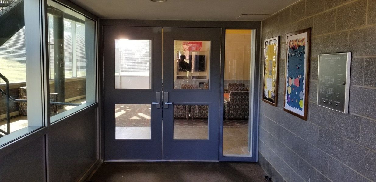 Hallway with double doors and large windows.  Grey brick walls with posters.