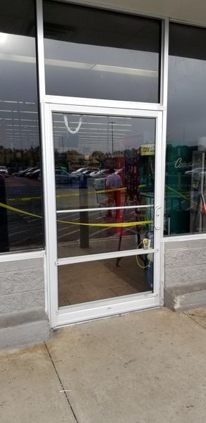 Closed glass door with yellow caution tape, reflecting a parking lot.