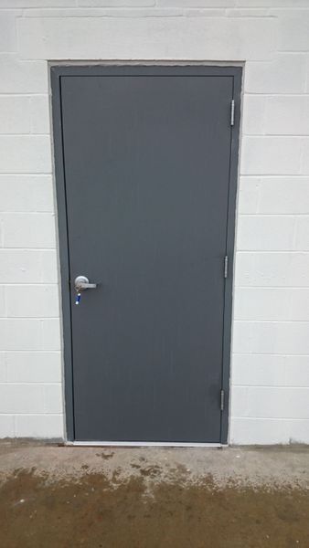 Gray door in a white brick wall. Door has a silver handle and hinges.