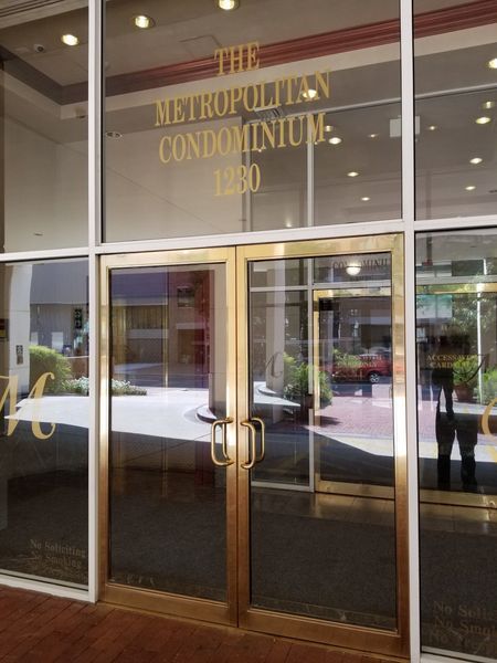 Entrance to The Metropolitan Condominium, with gold lettering and doors. Address: 1280. Light reflects off the glass.