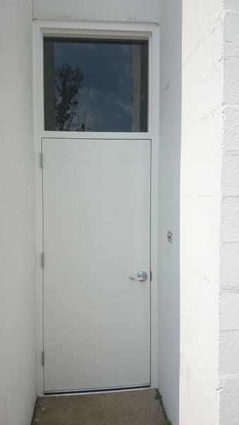 White door with a window above it, set in a white wall recess.