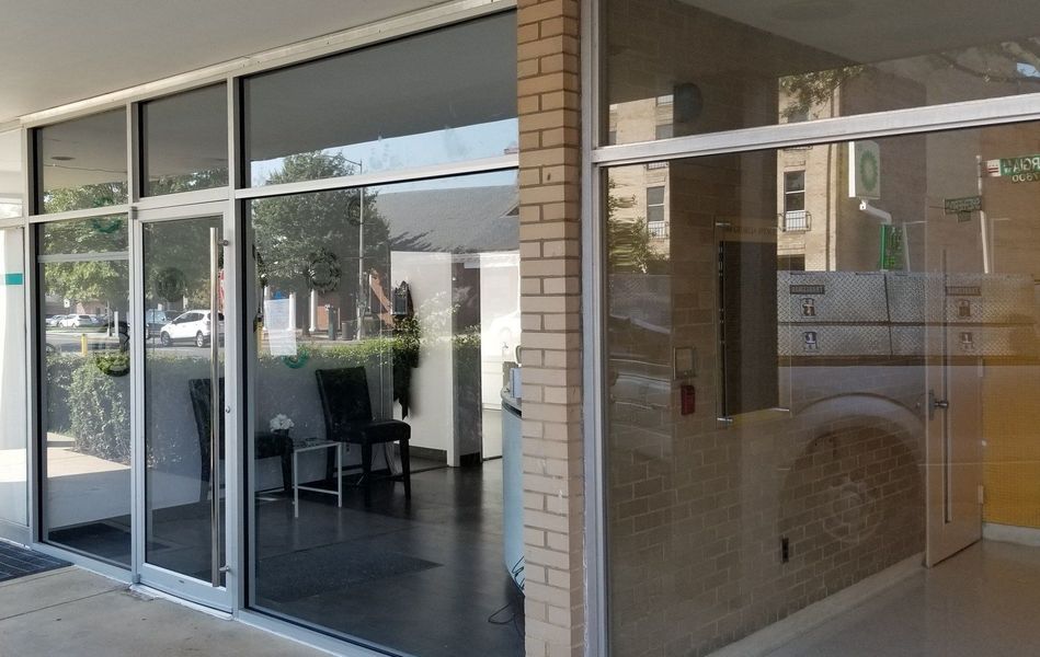 Exterior of a building with glass doors and windows reflecting the outside; brick and white trim.