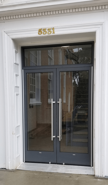 Double glass doors with silver handles, grey frames, and transom window; gold address numbers 