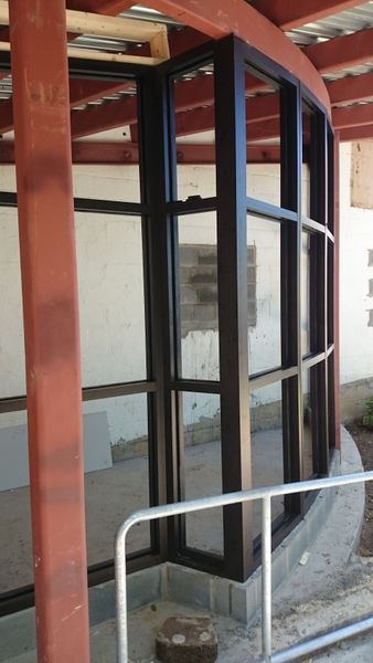 Black-framed, curved glass window installation in a partially constructed building. Red structural beam nearby.