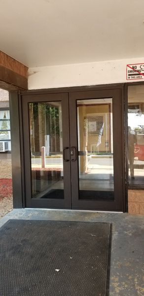 Double glass doors with dark frames, leading into a building. A black mat sits outside.