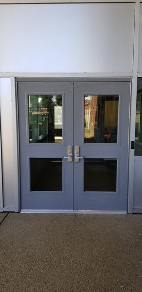 Double gray doors with glass panes and silver door handles in an exterior setting.