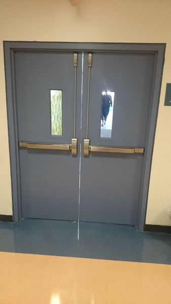 Double blue doors with push bars, small windows, and a reflection of a person.