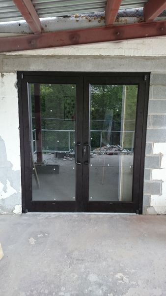 Dark-framed double doors with glass panels, set in a gray wall, reflecting an outdoor view.