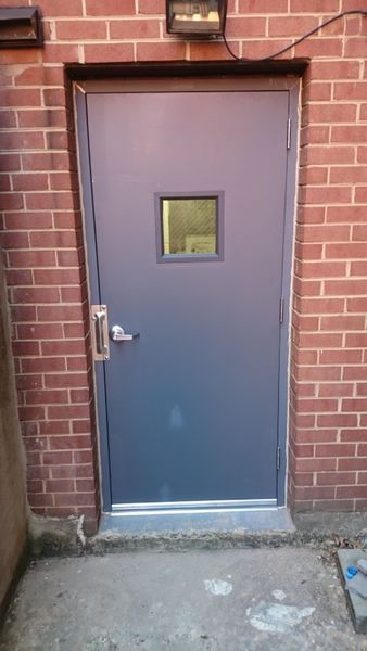 Grey door in brick wall with a small window, handle, and a light above.