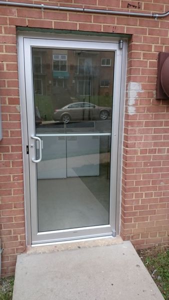 Glass door with silver frame set in a brick wall, concrete ramp leads to the door.