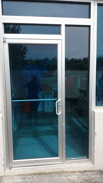 Blue-tinted glass door with a sidelight, framed in silver, set in a white wall.
