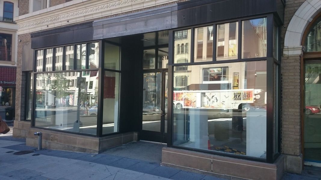 Empty storefront with large windows reflecting street scene and dark awning.