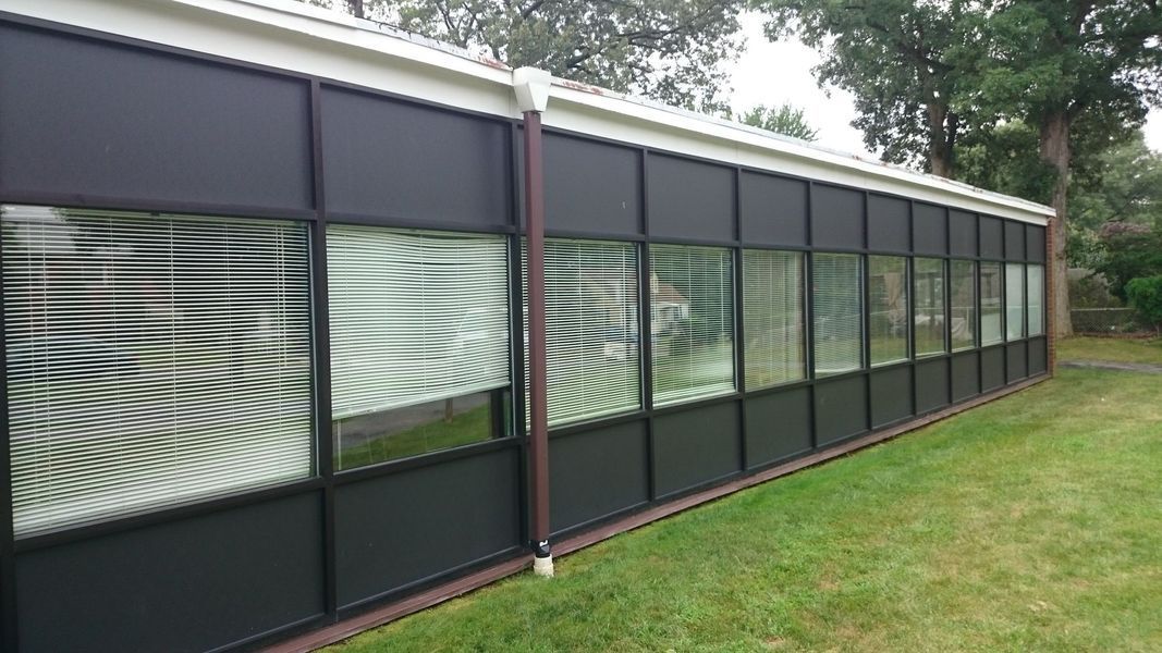 Black-framed windows in a long, modern building with white trim, set on green grass.