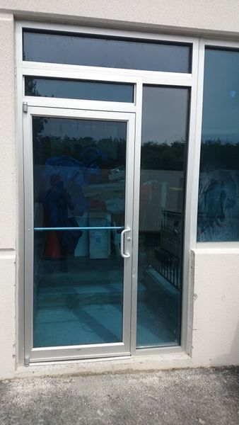 Aluminum-framed glass door with blue-tinted windows. Includes a side panel and transom window above.