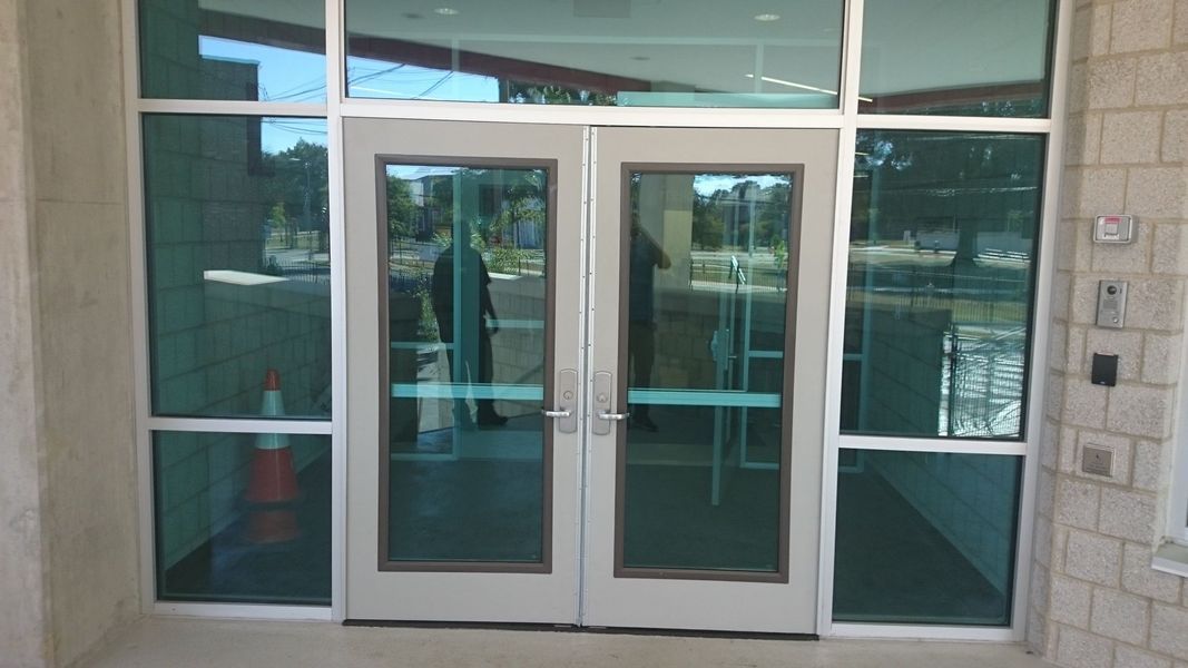 Double glass doors with side and top windows. Reflective green tint.  Building exterior.
