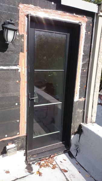 Black door with glass panes set in a dark frame, mounted on a rooftop with exposed construction materials.