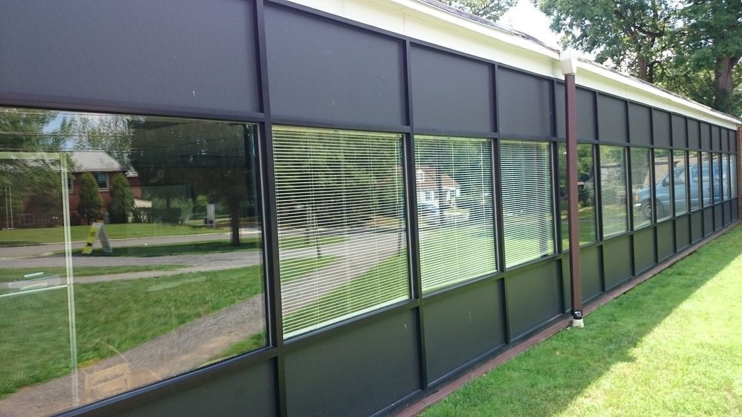 Long, dark building with glass windows; some have shades, others have blinds.