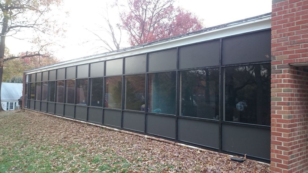 Long, windowed building with black frames and glass, set in a yard with fallen leaves.