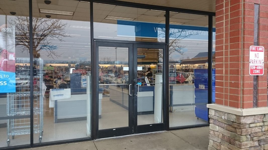 Storefront with glass doors, large windows, and items visible inside. Brick columns on the right.