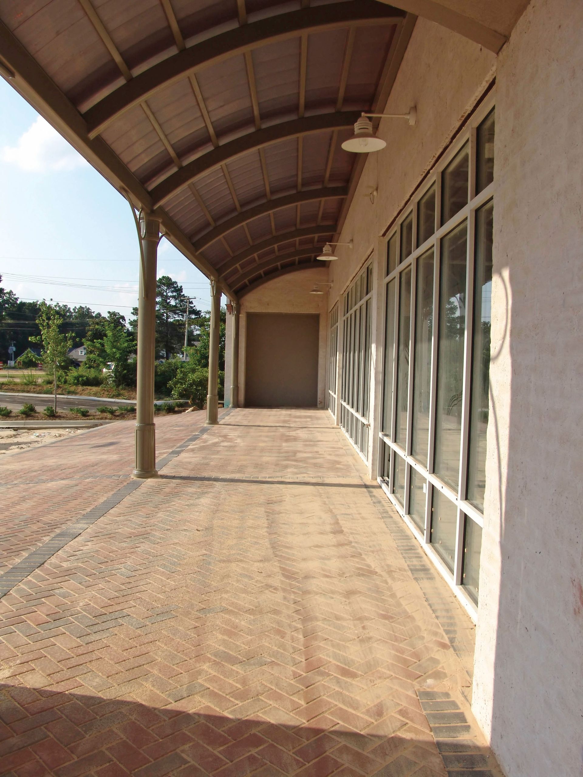 Covered walkway with brick pavers and large windows on a building exterior.
