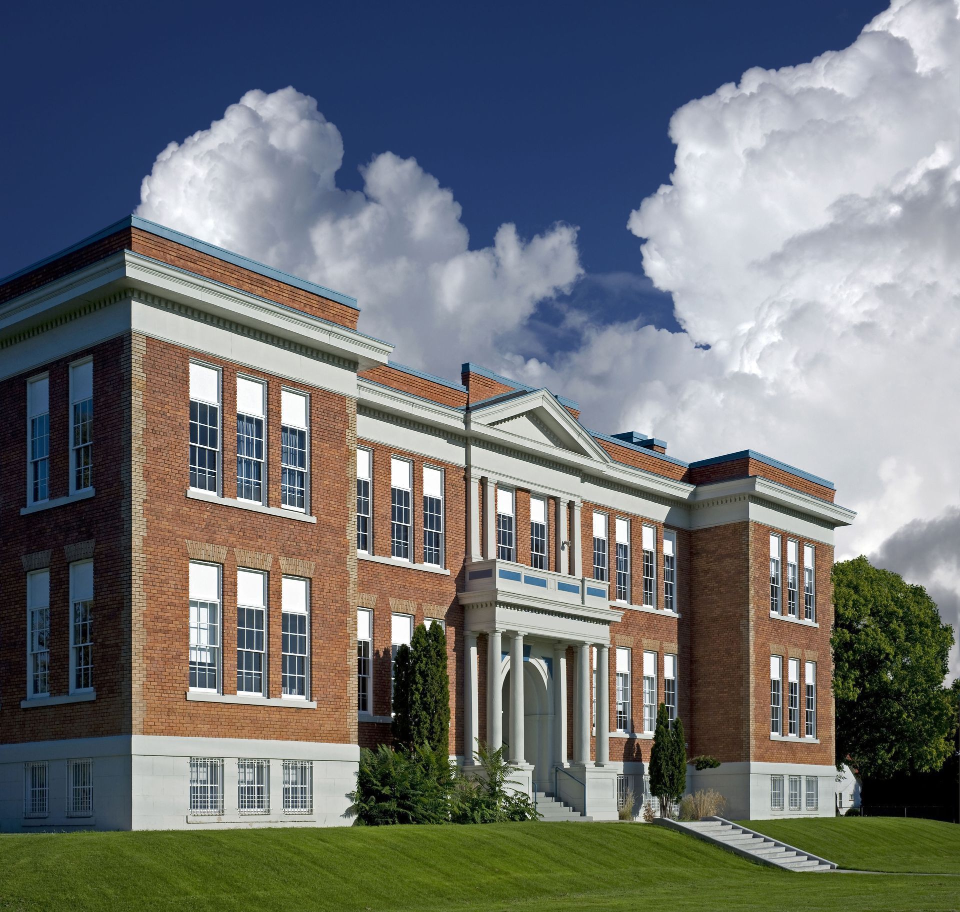 Brick school building with white trim, green lawn, and cloudy sky.