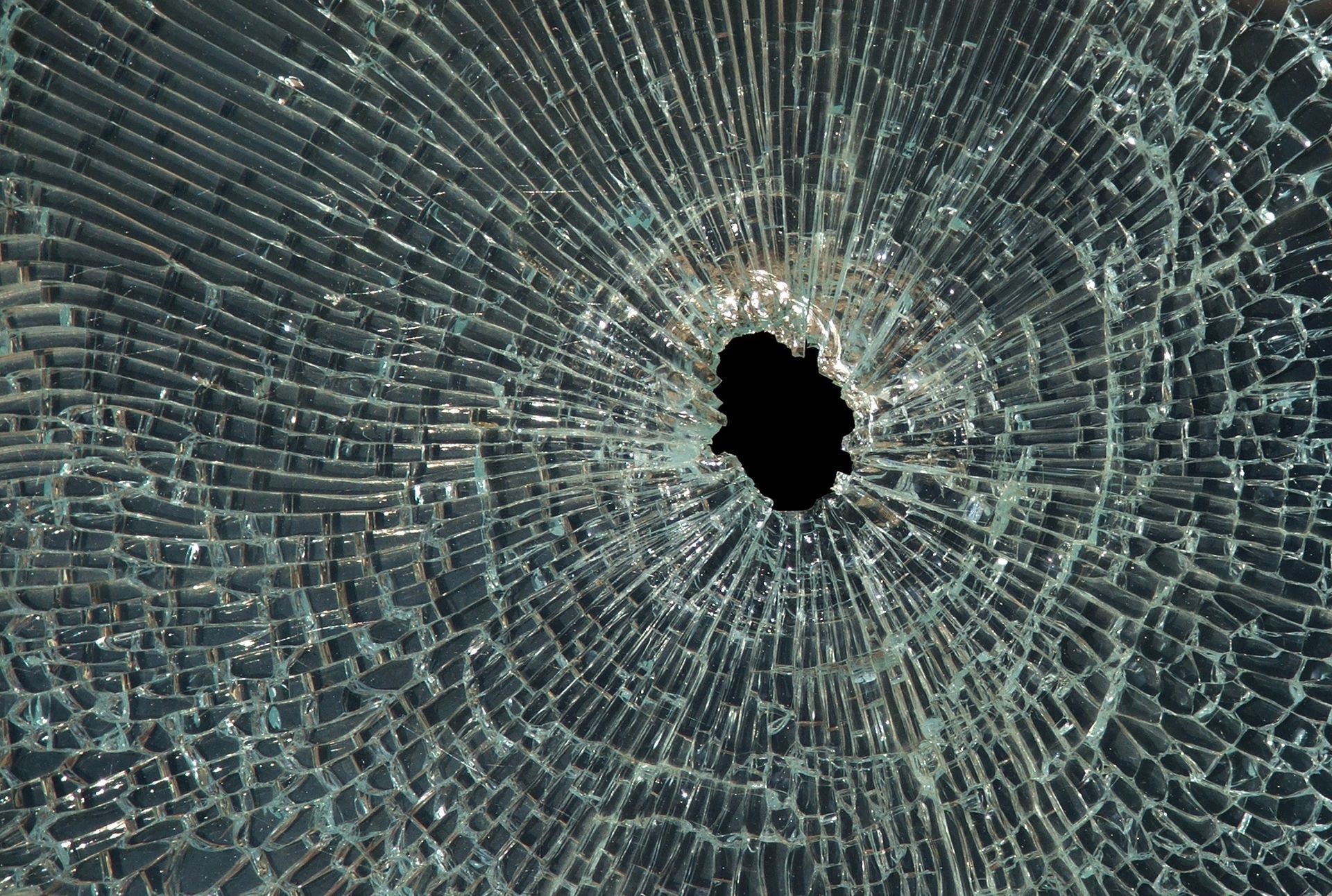 Shattered glass window with a central hole, radial cracks emanating outwards, black void.