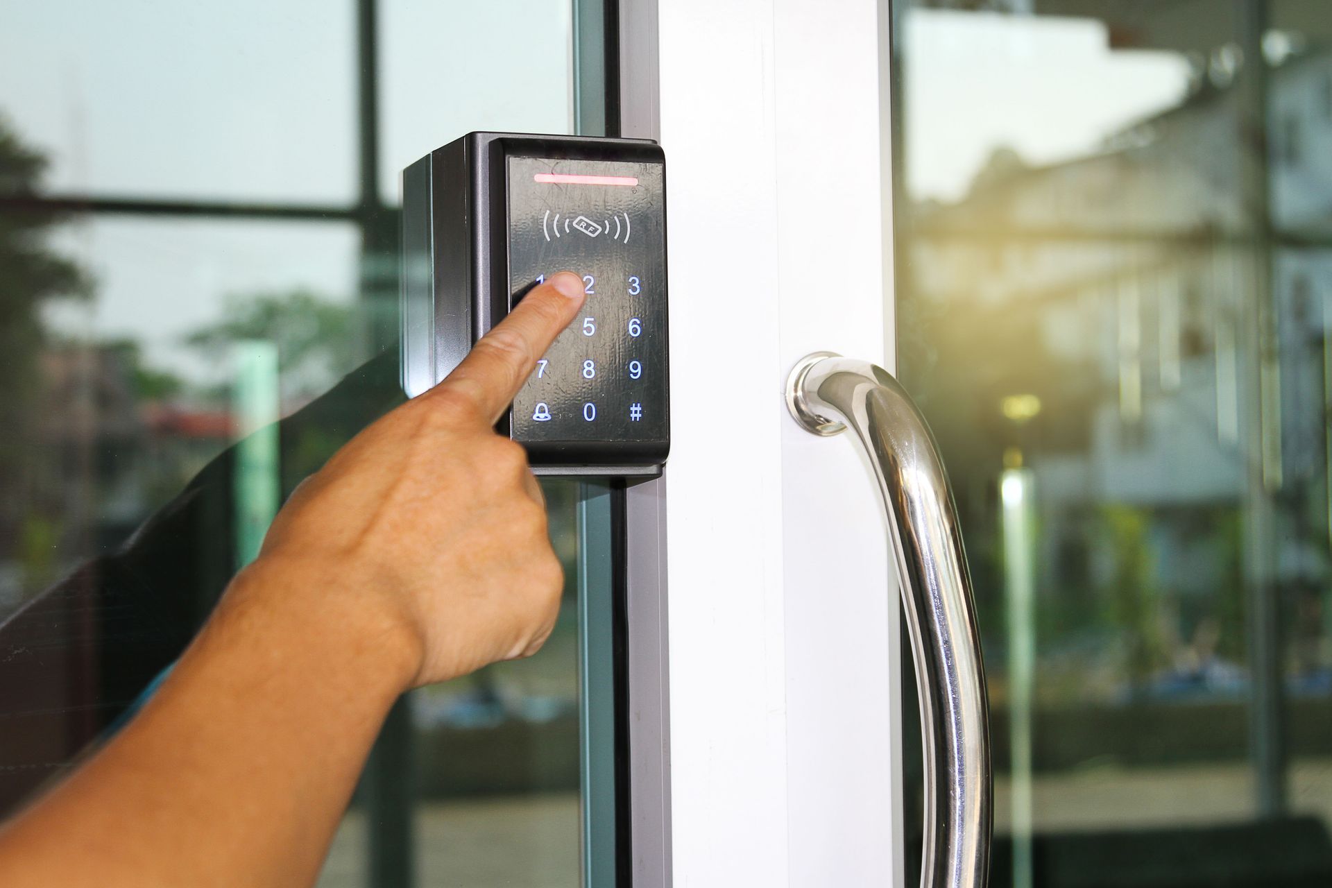 A person's hand pressing a keypad on a glass door, possibly entering a code for access.