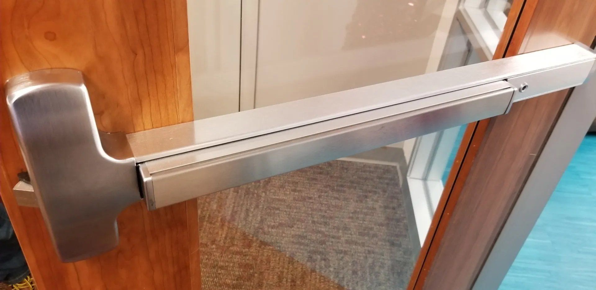 A silver crash bar on a wooden door, leading to a glass door frame.