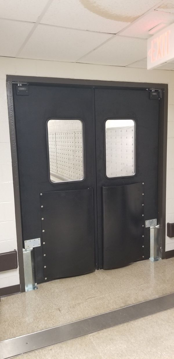 Black double doors with windows, supported by metal brackets, in a hallway.