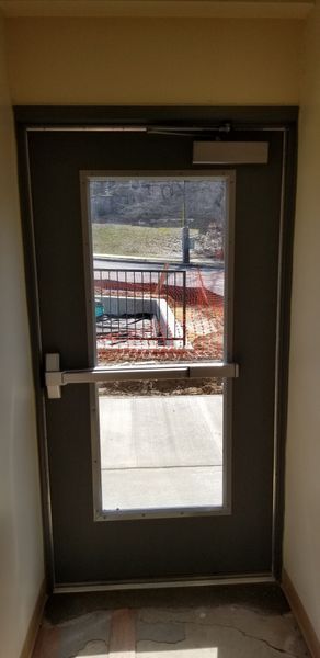 Exterior door with window. Gray door with silver hardware. Outside view of a concrete area.