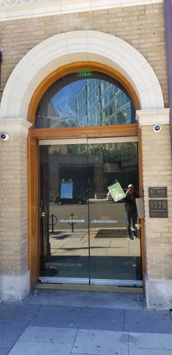 Entrance with arched window above glass doors, security cameras, and signs on the brick facade.