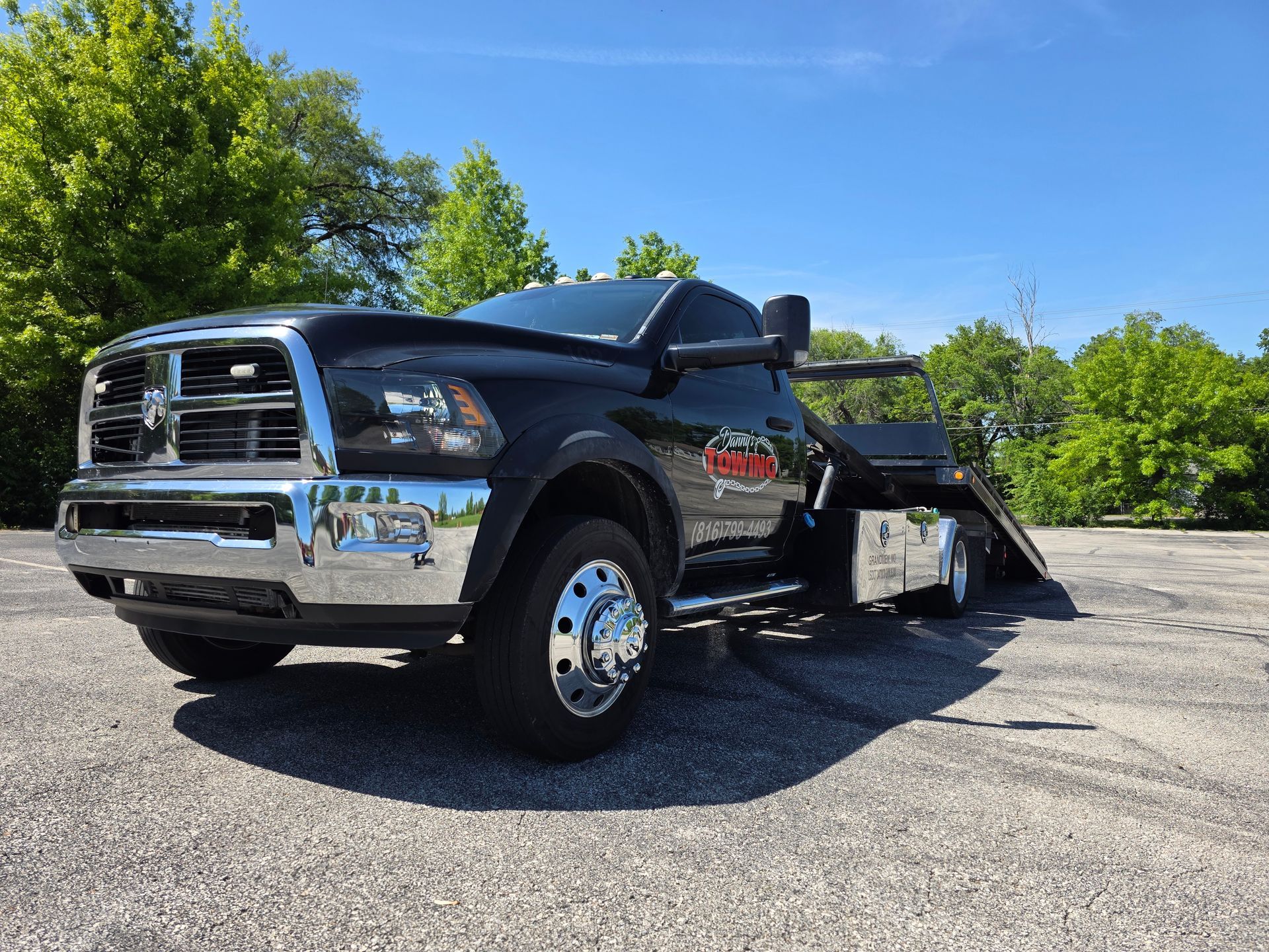 Black tow truck parked on asphalt on a sunny day with trees in the background.