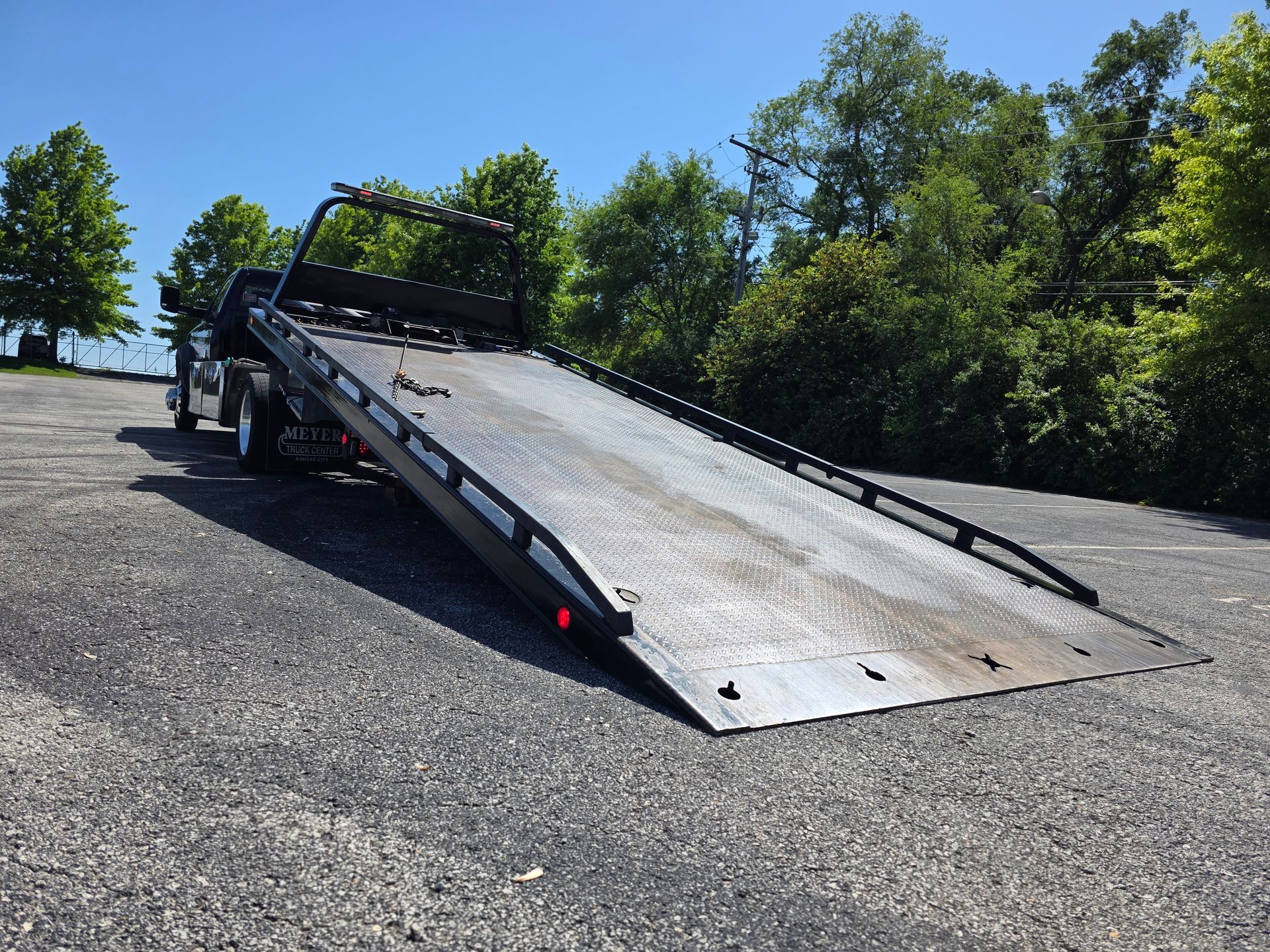 Tow truck with an extended flatbed, parked on asphalt, angled toward the viewer; blue sky.