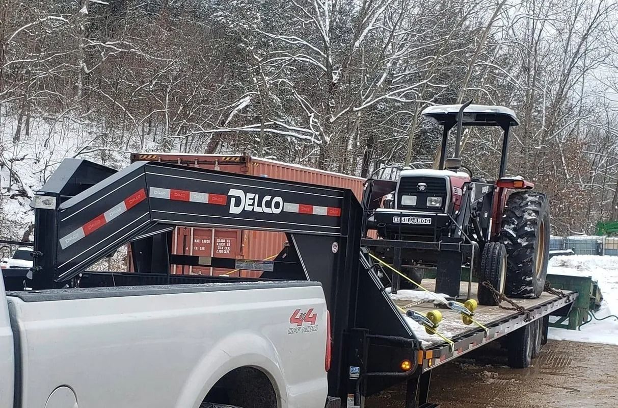 A white truck towing a flatbed trailer with a red tractor on it, set in a snowy outdoor scene.