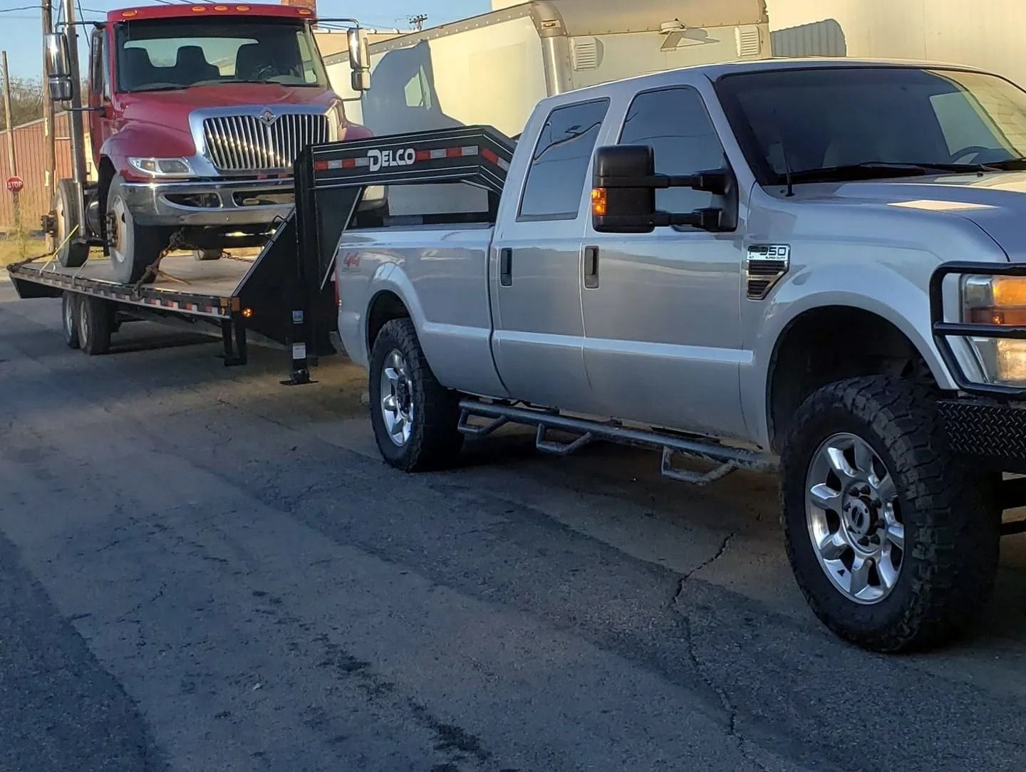Silver pickup truck towing a red tow truck on a black trailer on a paved road.