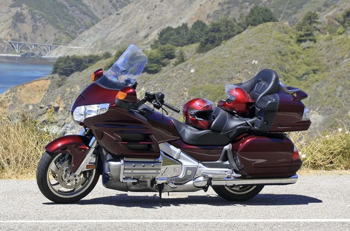 Red Honda Goldwing motorcycle parked on a roadside overlooking a bridge and ocean.