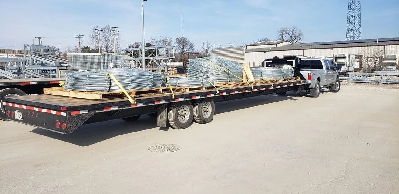 Truck hauling pallets of metal materials on a flatbed trailer, outdoors under a blue sky.