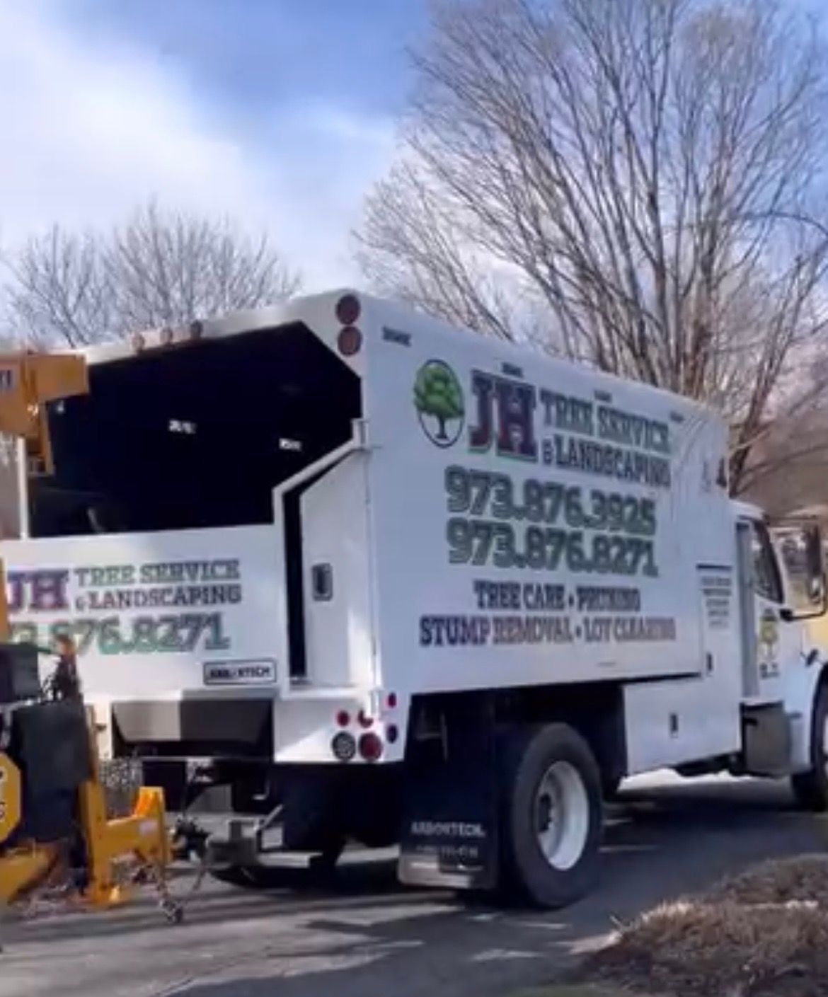 White JH Tree Service truck parked on a driveway with a wood chipper nearby.