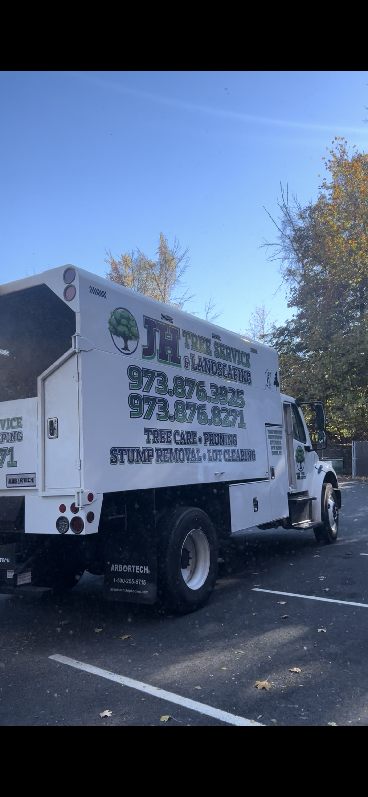 A white tree service truck parked in a parking lot on a sunny day.