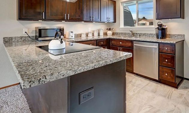 Modern kitchen with granite island, dark wood cabinets, stainless steel appliances, and a window over the sink