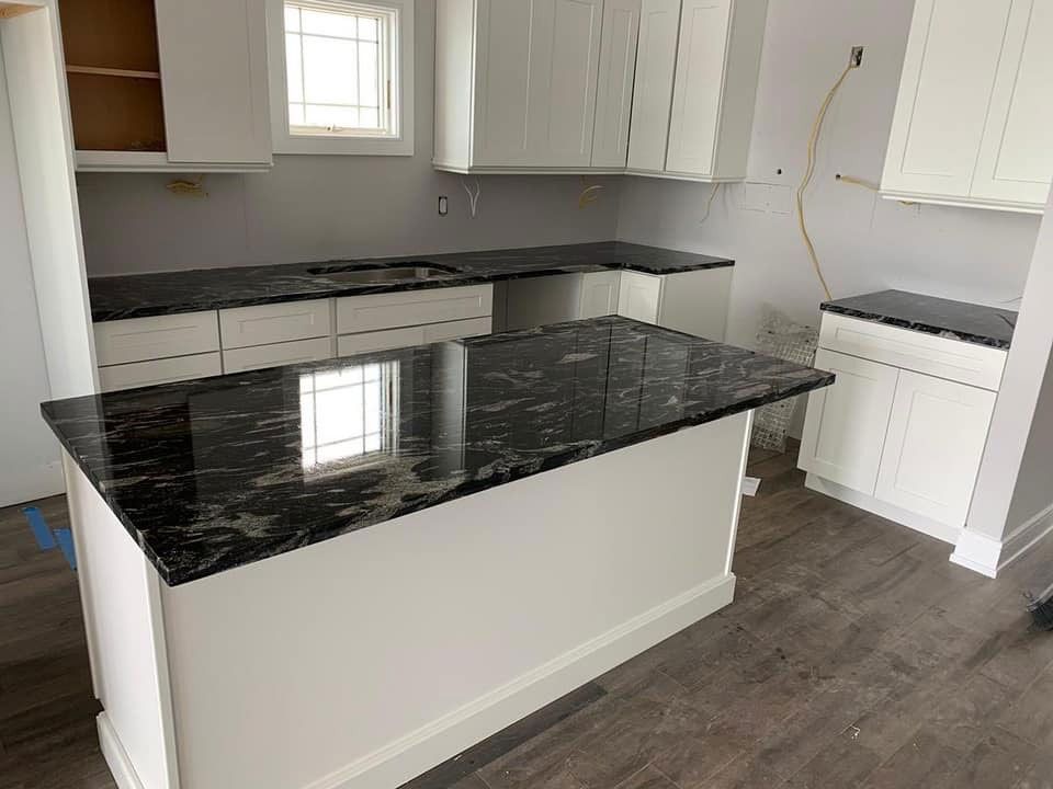 Modern kitchen with white cabinets, dark countertops, and a black marble island in a bright room