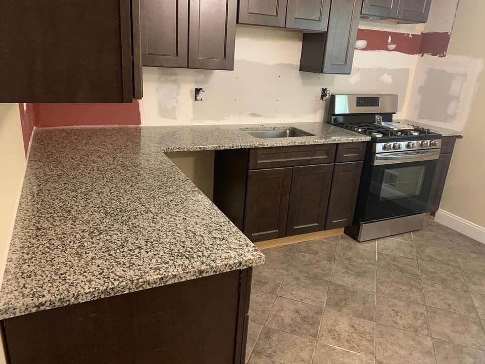 Empty kitchen with granite countertops, dark wood cabinets, and a stainless steel stove on tile flooring