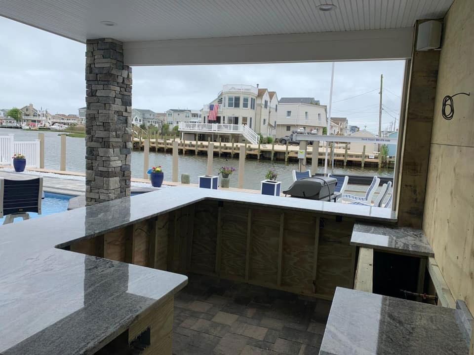 Covered outdoor bar overlooking a marina with stone counters and water in the background