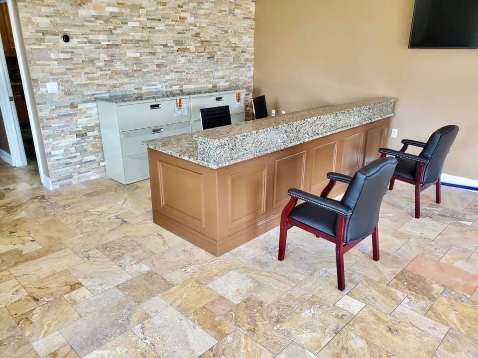 Lobby with stone wall, wood-and-stone reception desk, and two chairs on a tiled floor.