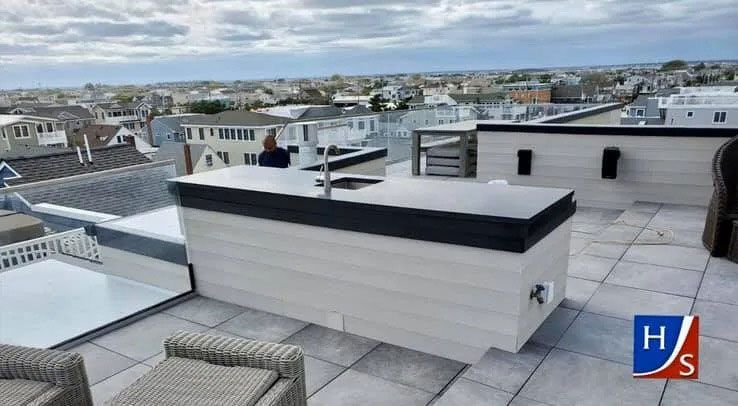 Rooftop terrace with white and black structures, city houses in the distance under a cloudy sky