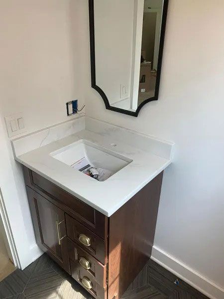 Small bathroom vanity with white sink and dark wood cabinet beneath a mirror.