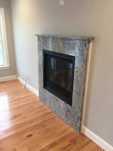 Gray stone fireplace with a black insert in a light-walled room with hardwood floors