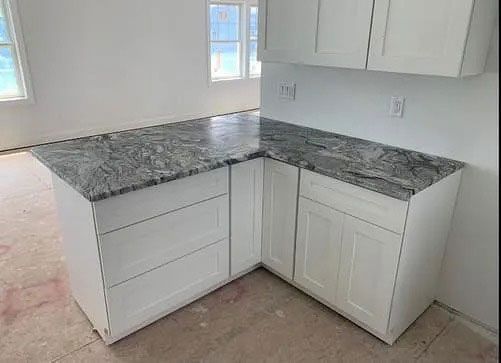 Empty white kitchen corner with gray granite countertop and white cabinets under installation