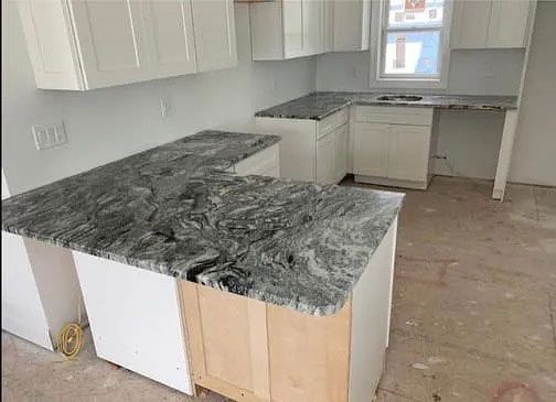 Unfinished kitchen with white cabinets and dark granite countertops under installation.
