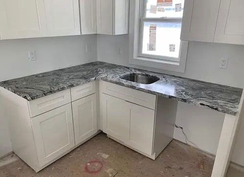 Small kitchen with white cabinets, granite countertops, and a stainless sink by a window.